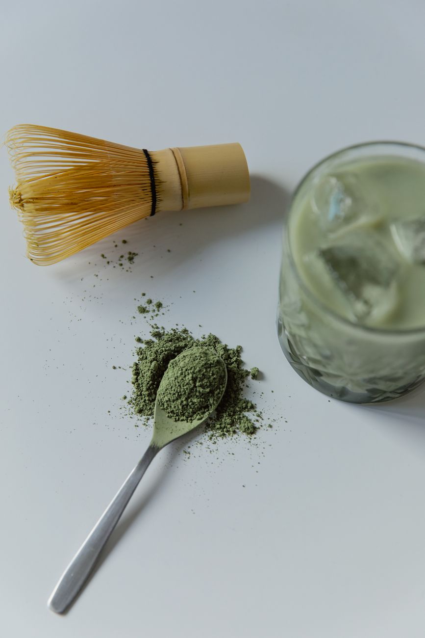 Vibrant green fukamushicha tea leaves with fine broken particles next to brewed deep-steamed sencha in a ceramic cup.