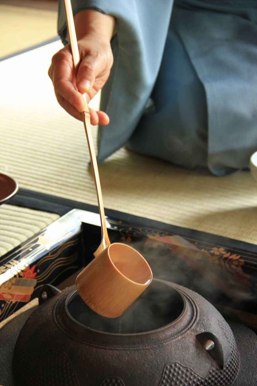 Traditional Japanese tea ceremony host whisking matcha in ceramic bowl during formal chado practice in tatami room.