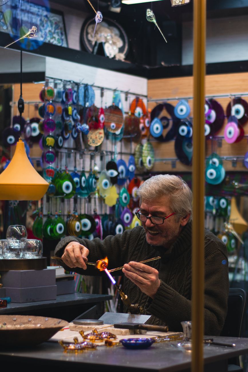Artisan heating molten glass over flame to shape a delicate blue drinking vessel in traditional Japanese workshop.