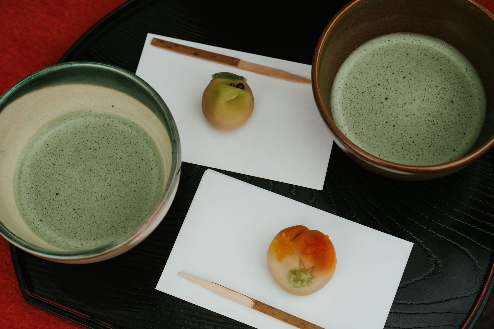 Weathered ceramic tea bowl with natural crack repairs sits on aged wooden surface beside bamboo tea whisk in dim light.