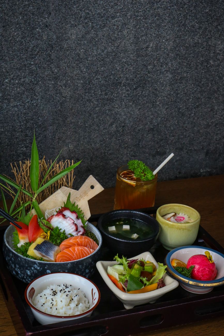Traditional Japanese meal arrangement showing a bowl of miso soup, rice, grilled fish, pickled vegetables, and simmered vegetables on a wooden tray.