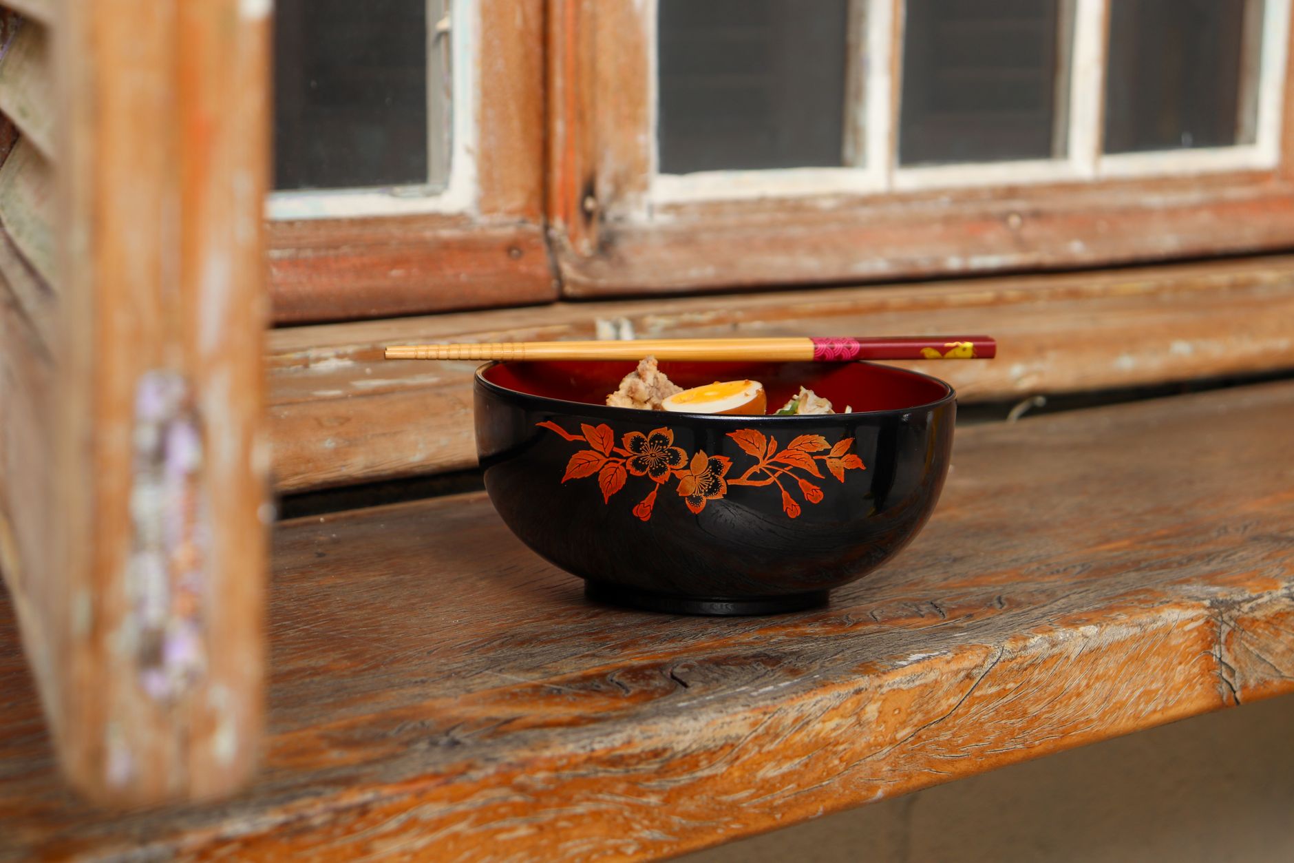 Black and red Japanese lacquerware bowls and plates arranged on a wooden dining table with chopsticks resting beside them.