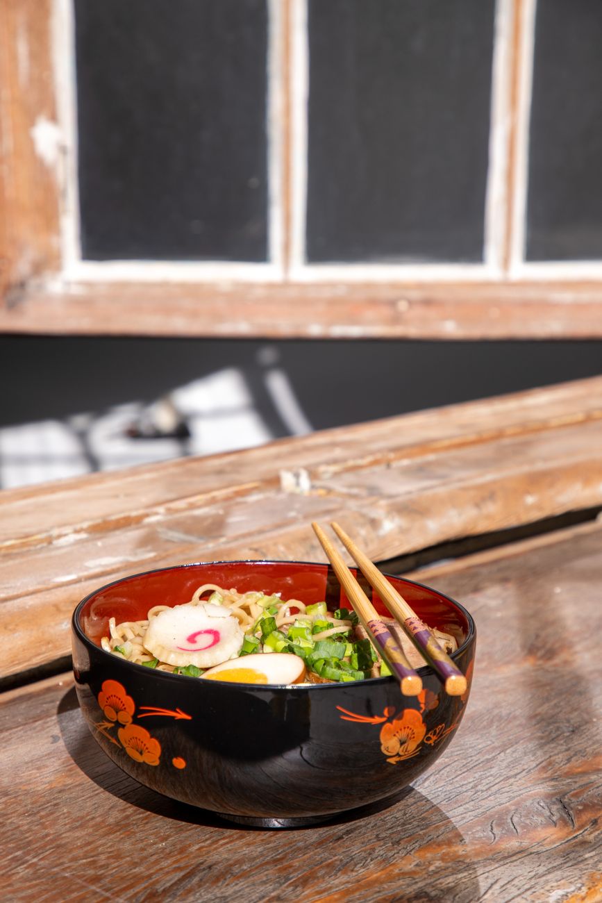 Black and red Japanese lacquerware bowls and plates arranged on a wooden dining table with chopsticks resting beside them.