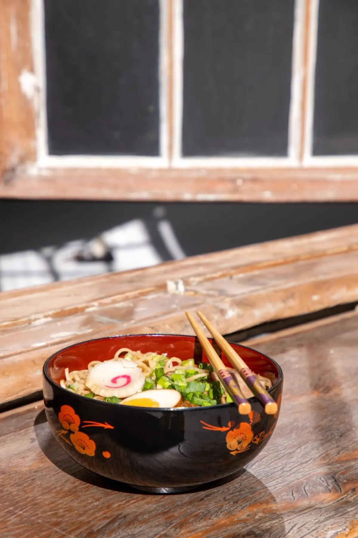 Black and red Japanese lacquerware bowls and plates arranged on a wooden dining table with chopsticks resting beside them.
