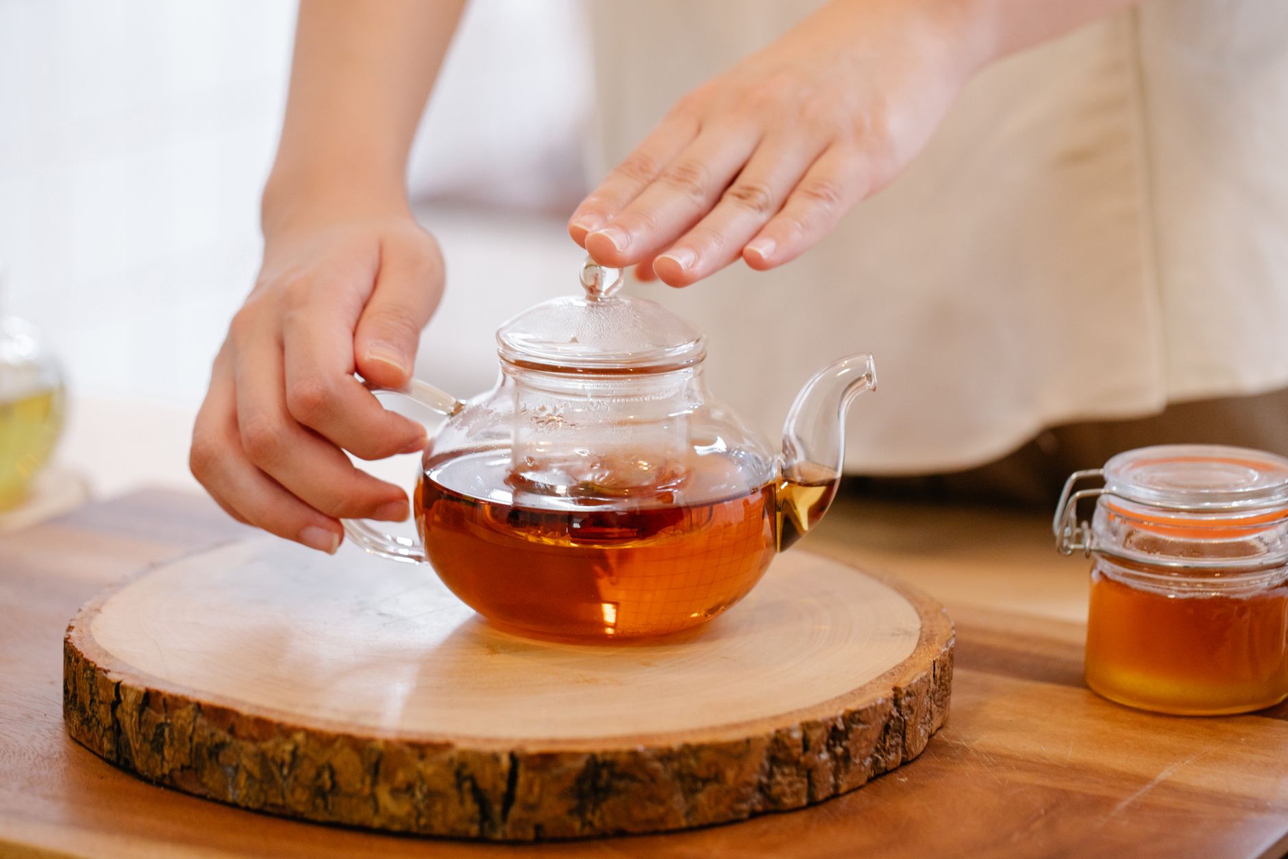 Fresh green tea leaves in a bamboo basket beside dark oxidized black tea leaves on a wooden table.