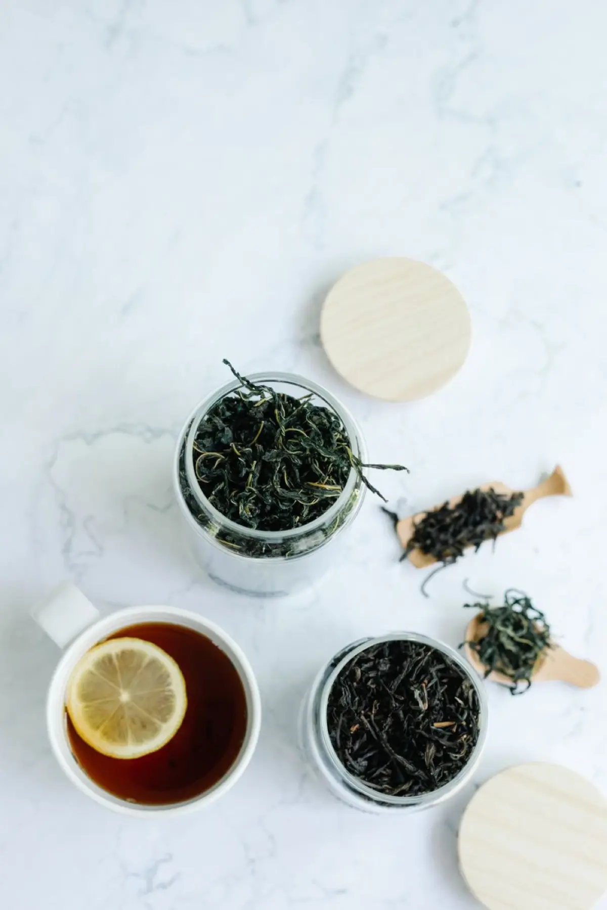 Fresh green tea leaves in a bamboo basket beside dark oxidized black tea leaves on a wooden table.