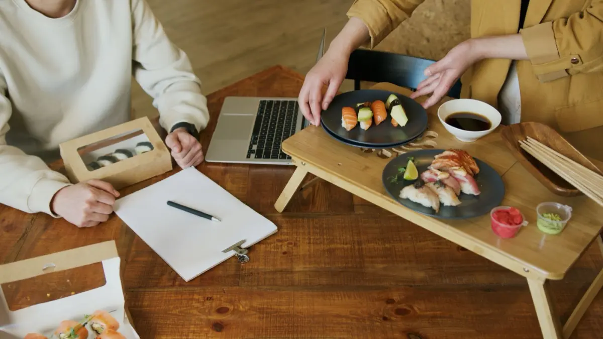 Ceramic bowl with autumn leaf motif holding grilled fish beside smaller dishes on wooden tray in traditional kaiseki setting.