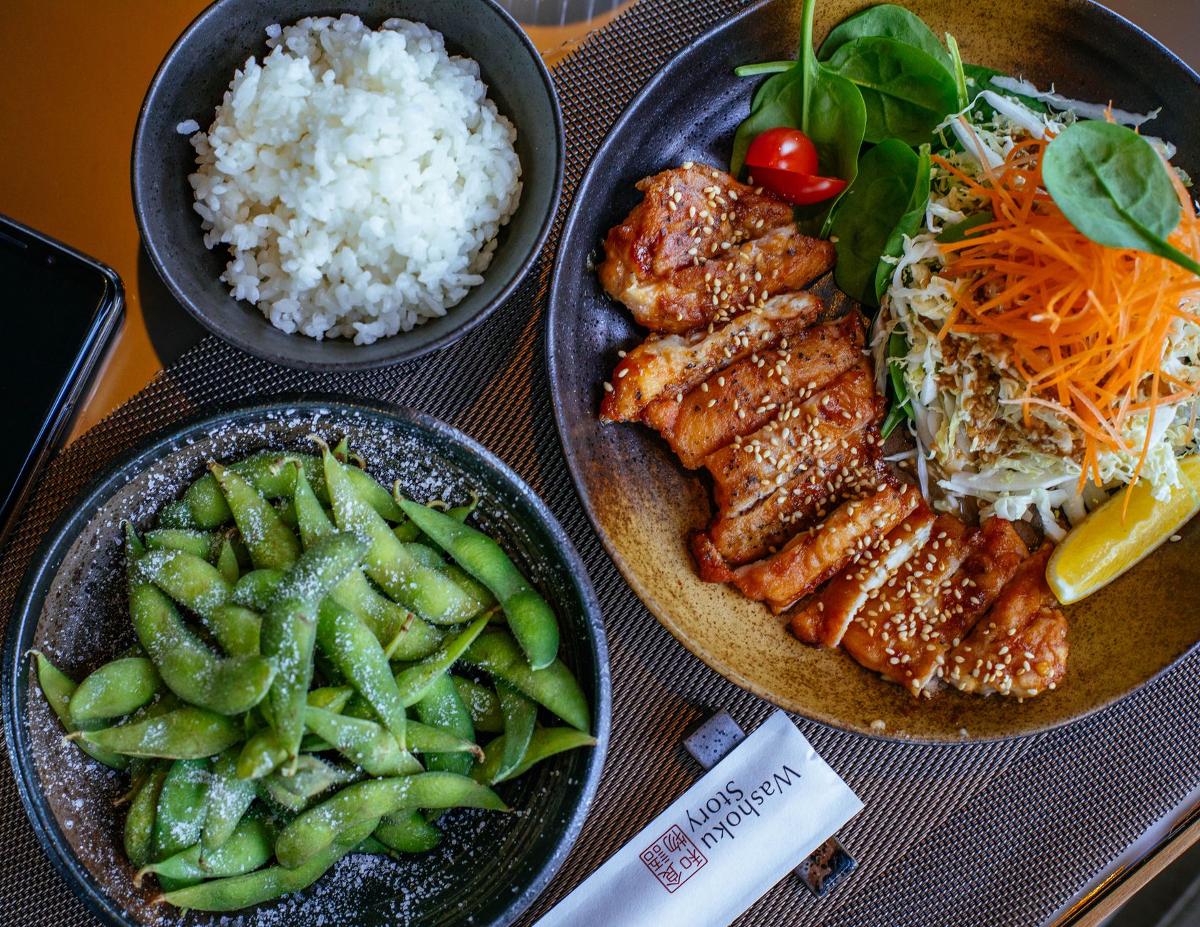 Hands gently cupping a traditional Japanese rice bowl at chest height during a meal with chopsticks resting nearby.