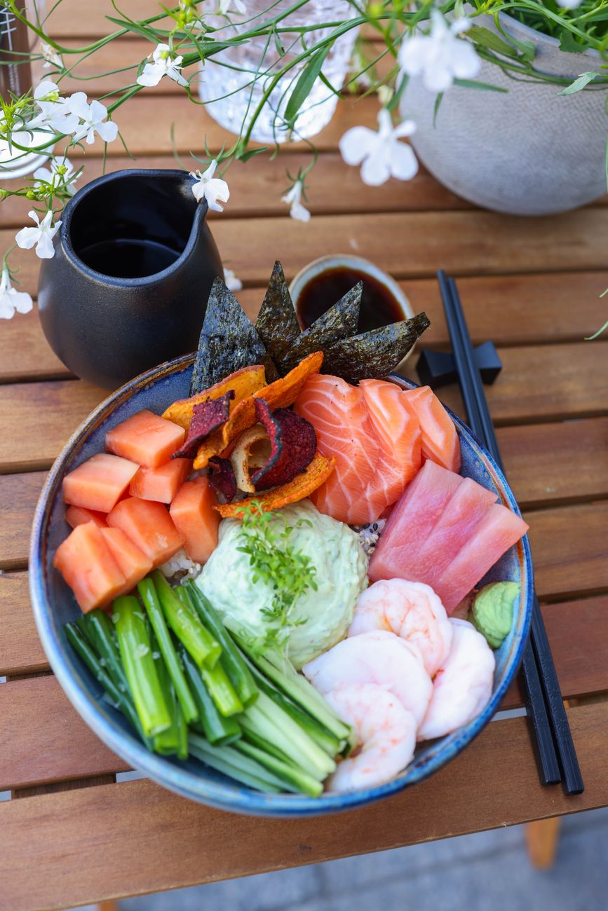 Hands gently cupping a traditional Japanese rice bowl at chest height during a meal with chopsticks resting nearby.