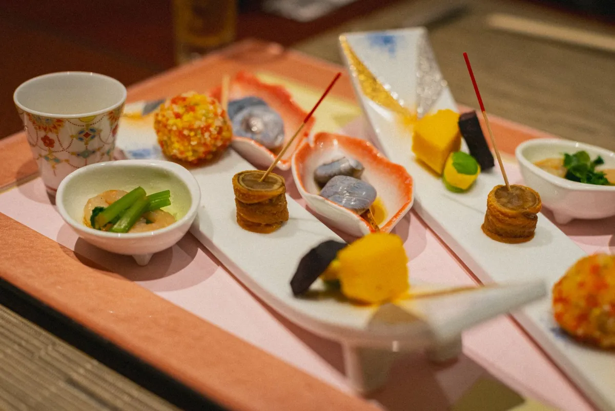 Minimalist kaiseki course presentation showing seasonal ingredients arranged on black lacquerware with negative space and natural garnishes.