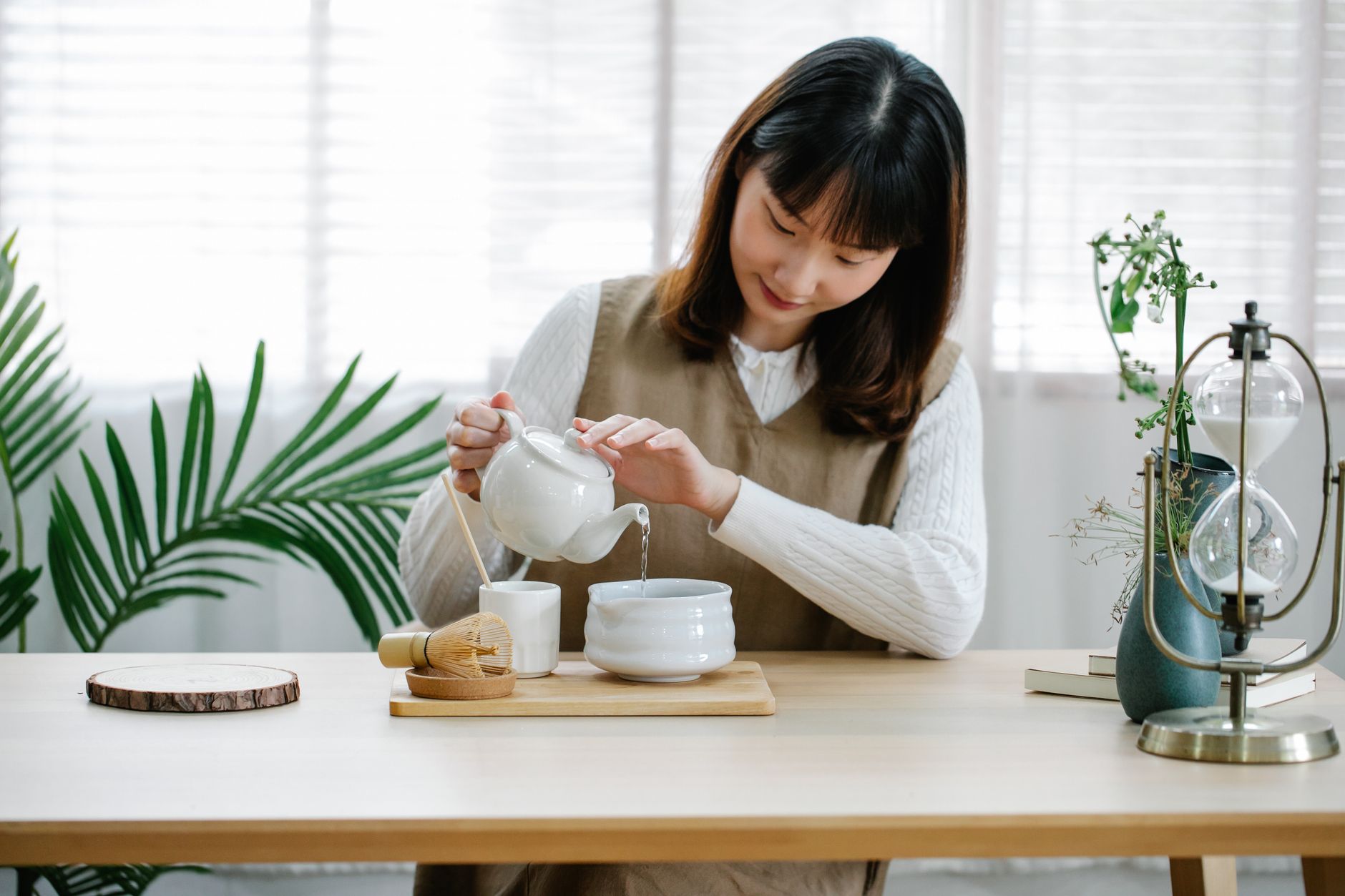 Two ceramic teacups on wooden table, one containing amber hojicha and the other pale green genmaicha with visible rice grains.