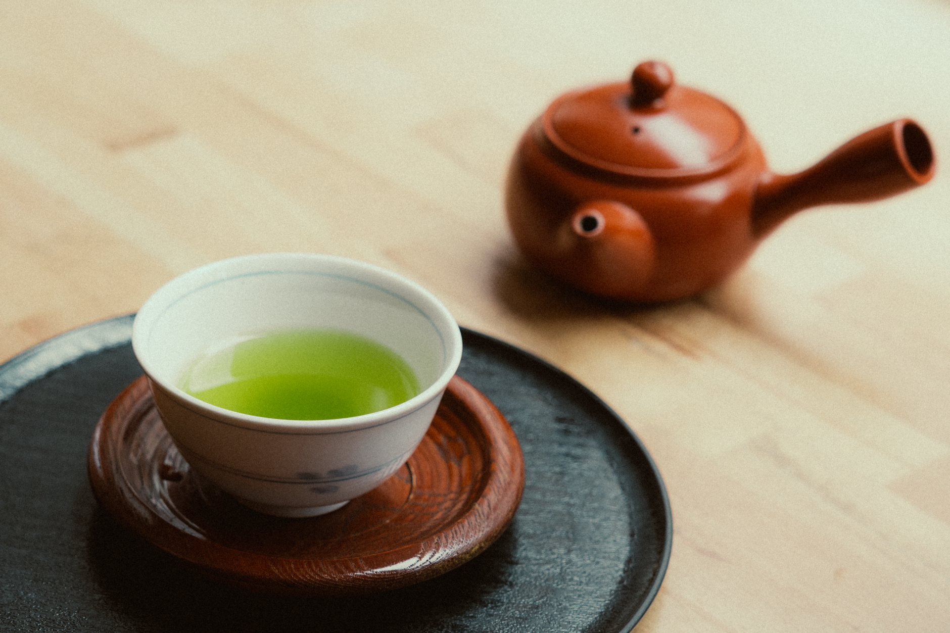 Side-by-side comparison showing Japanese green tea in a ceramic bowl beside Chinese oolong tea in a small porcelain cup.