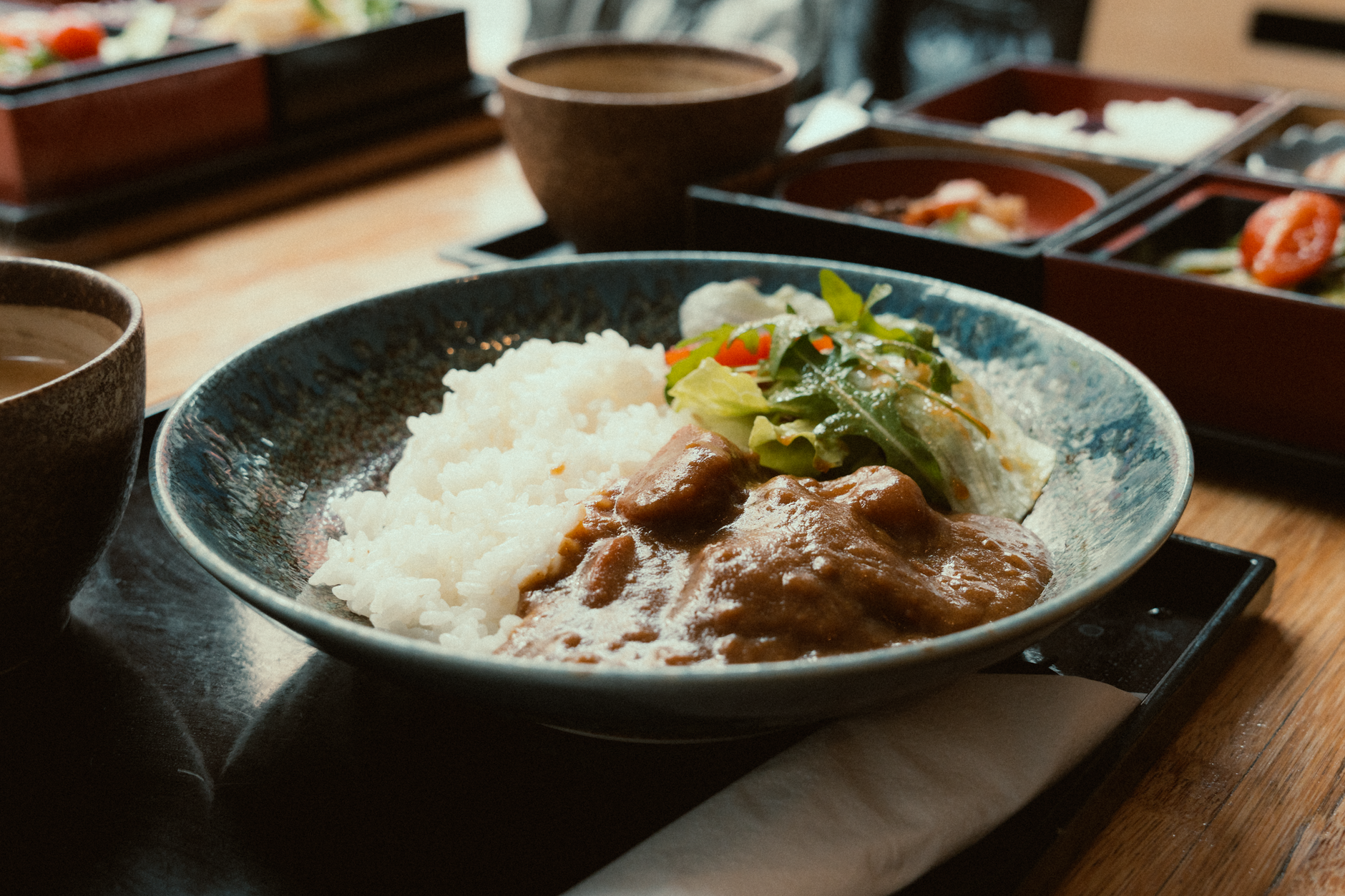 Ceramic plate with grilled fish positioned off-center, garnished with seasonal vegetables arranged in deliberate asymmetrical balance following Japanese aesthetic principles.