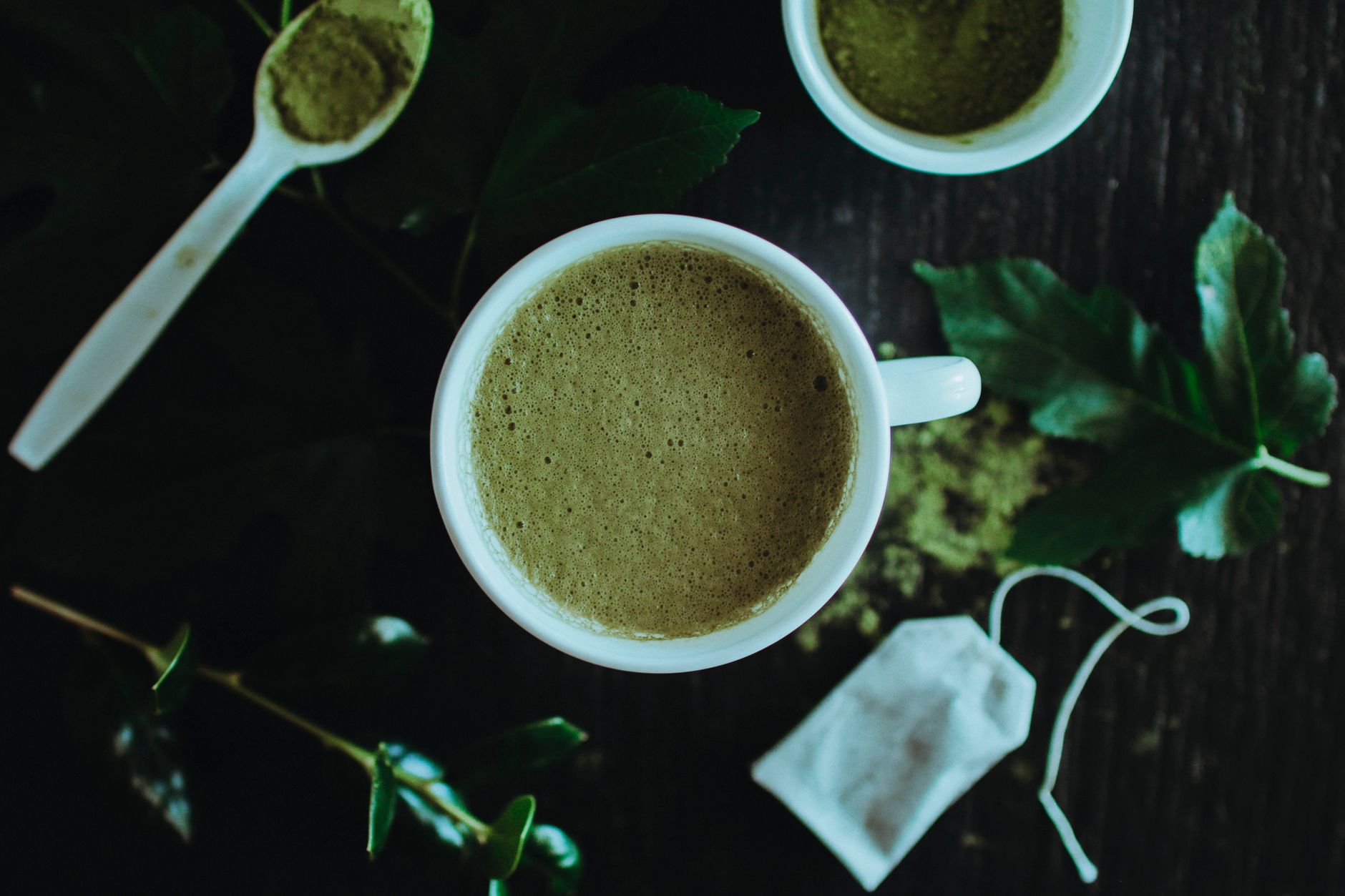 Two wooden scoops holding bright green ceremonial matcha powder beside duller culinary grade matcha on bamboo mat.