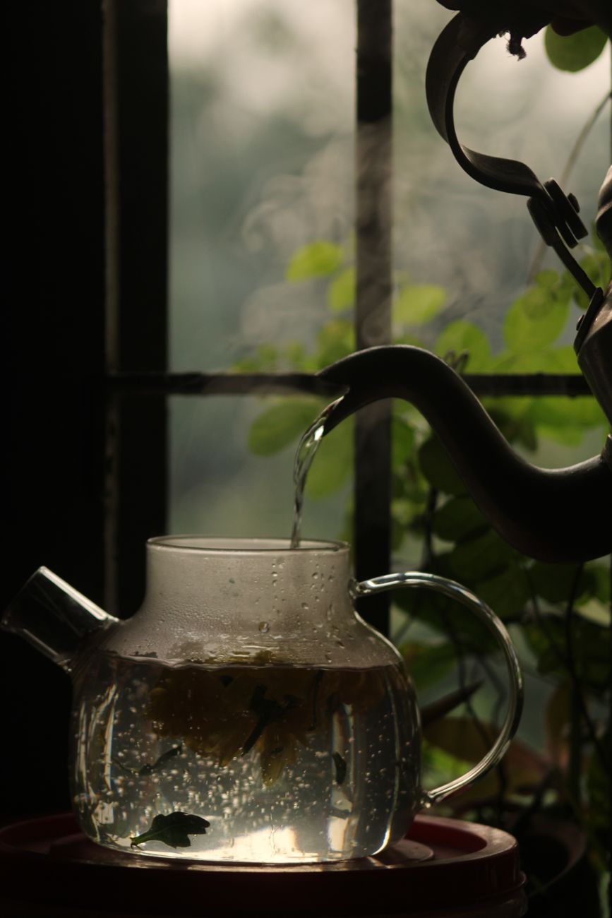 Fresh green tea leaves resting in a traditional bamboo steaming basket above gently rising steam in a Japanese tea workshop.
