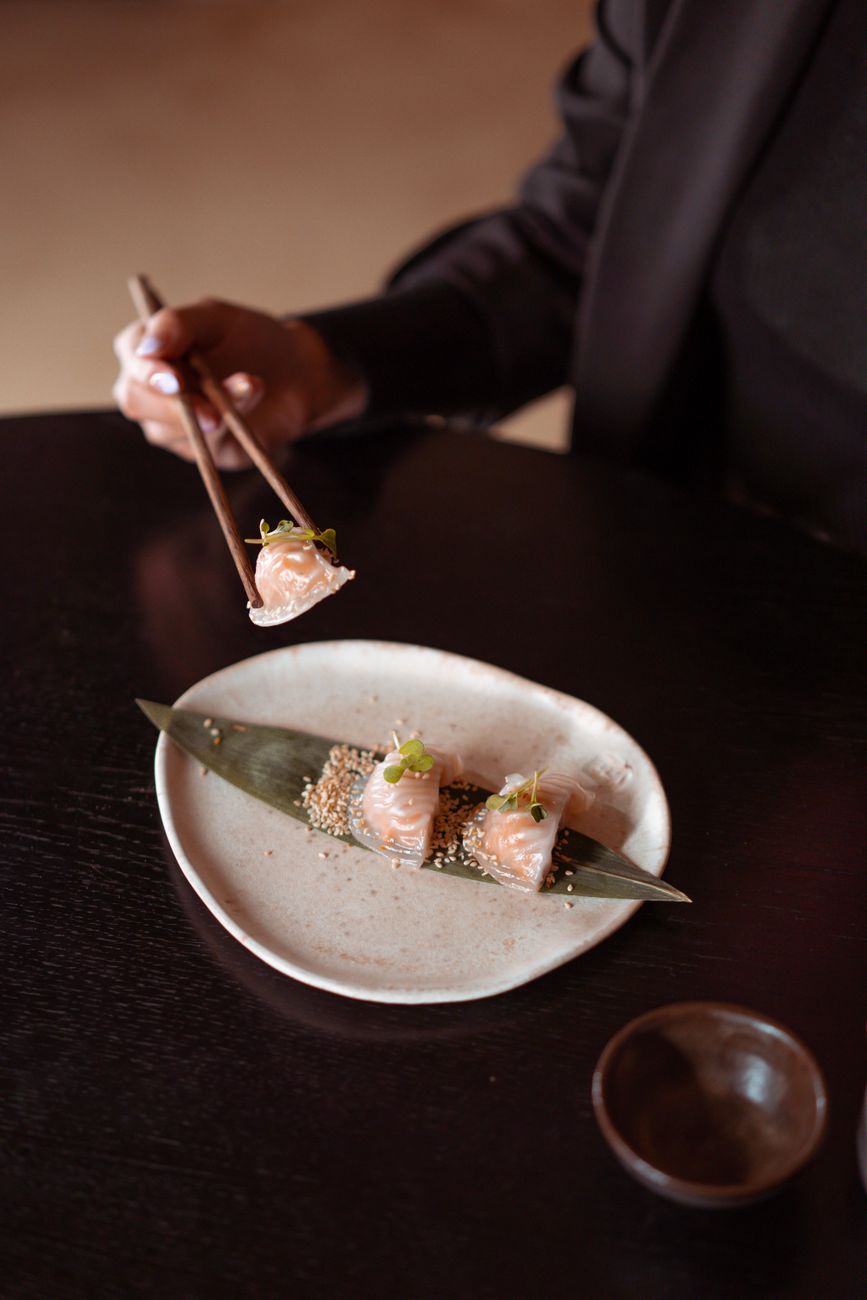 Thinly sliced tuna and salmon arranged in precise diagonal rows with shiso leaves and daikon garnish on white ceramic.