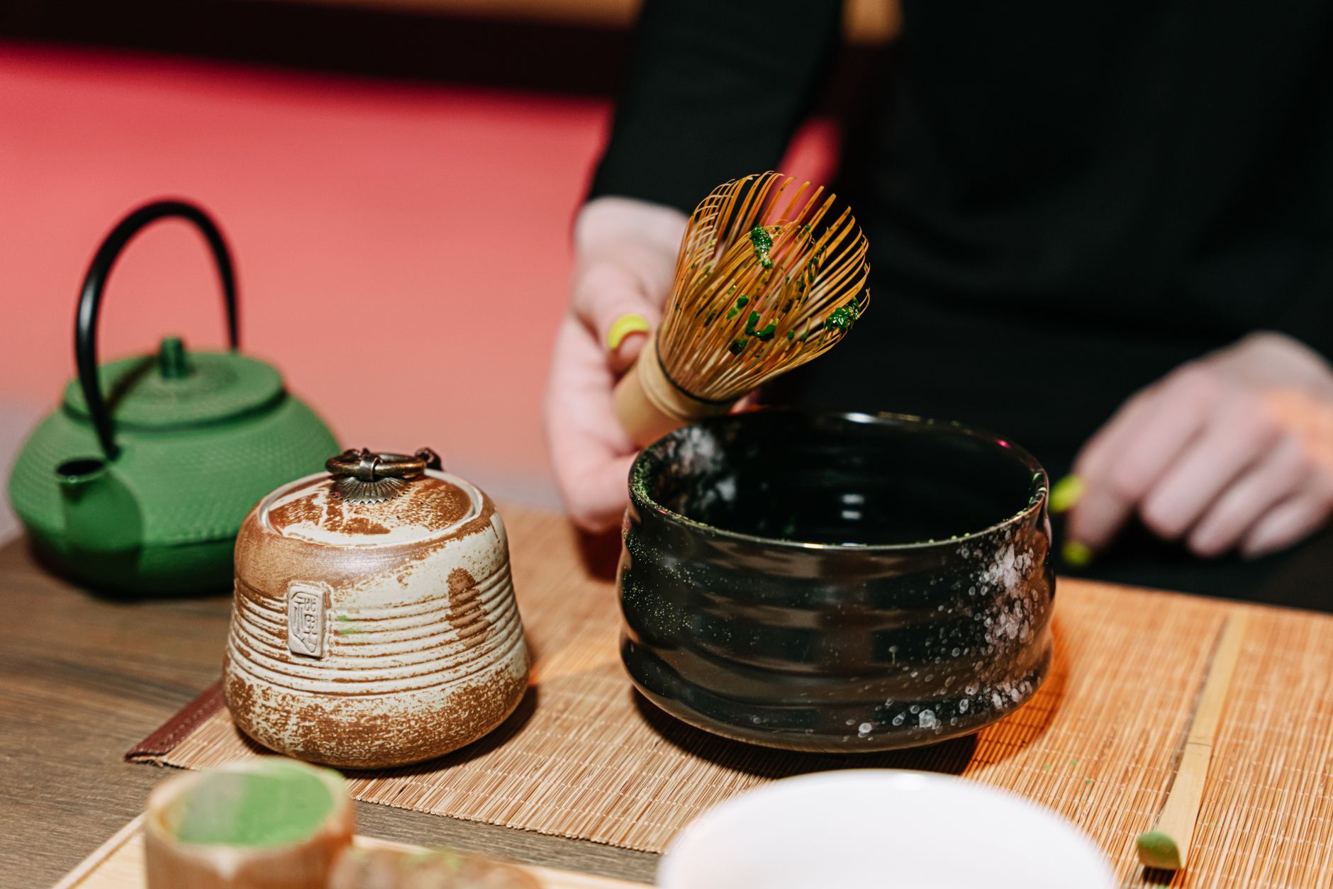 Traditional bamboo chasen with fine curved prongs next to a modern metal kitchen whisk on a tea preparation surface.