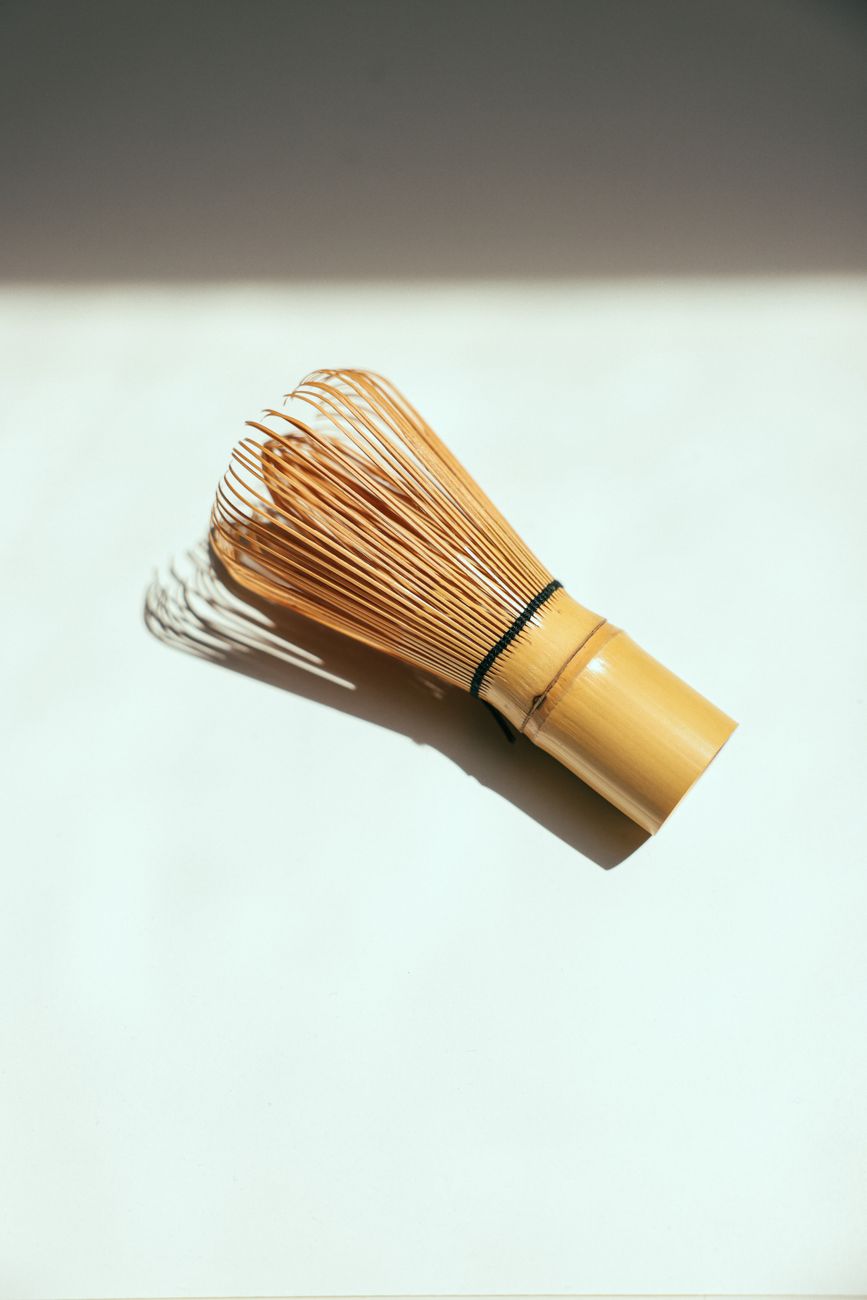 Traditional bamboo chasen with fine curved prongs next to a modern metal kitchen whisk on a tea preparation surface.