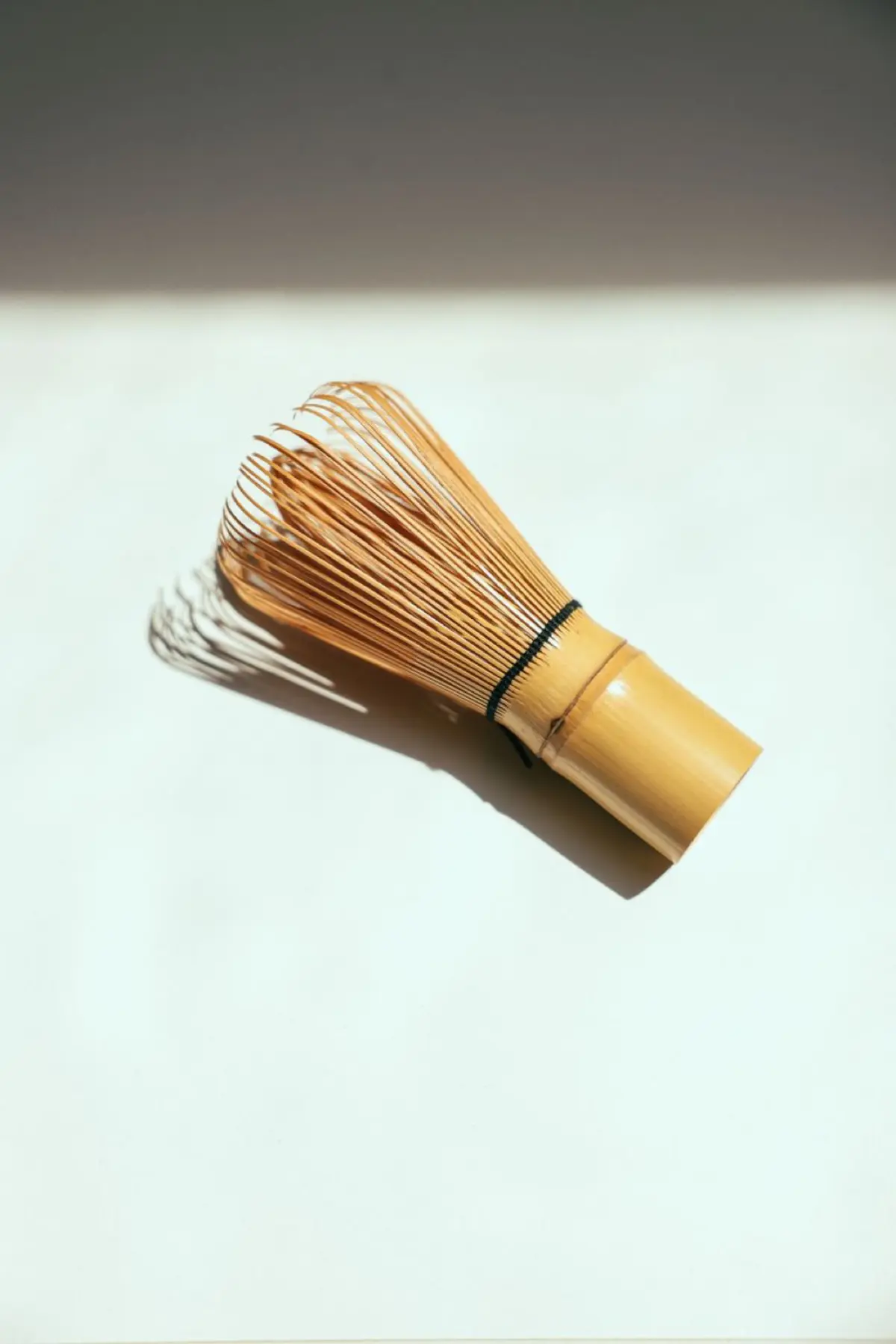 Traditional bamboo chasen with fine curved prongs next to a modern metal kitchen whisk on a tea preparation surface.