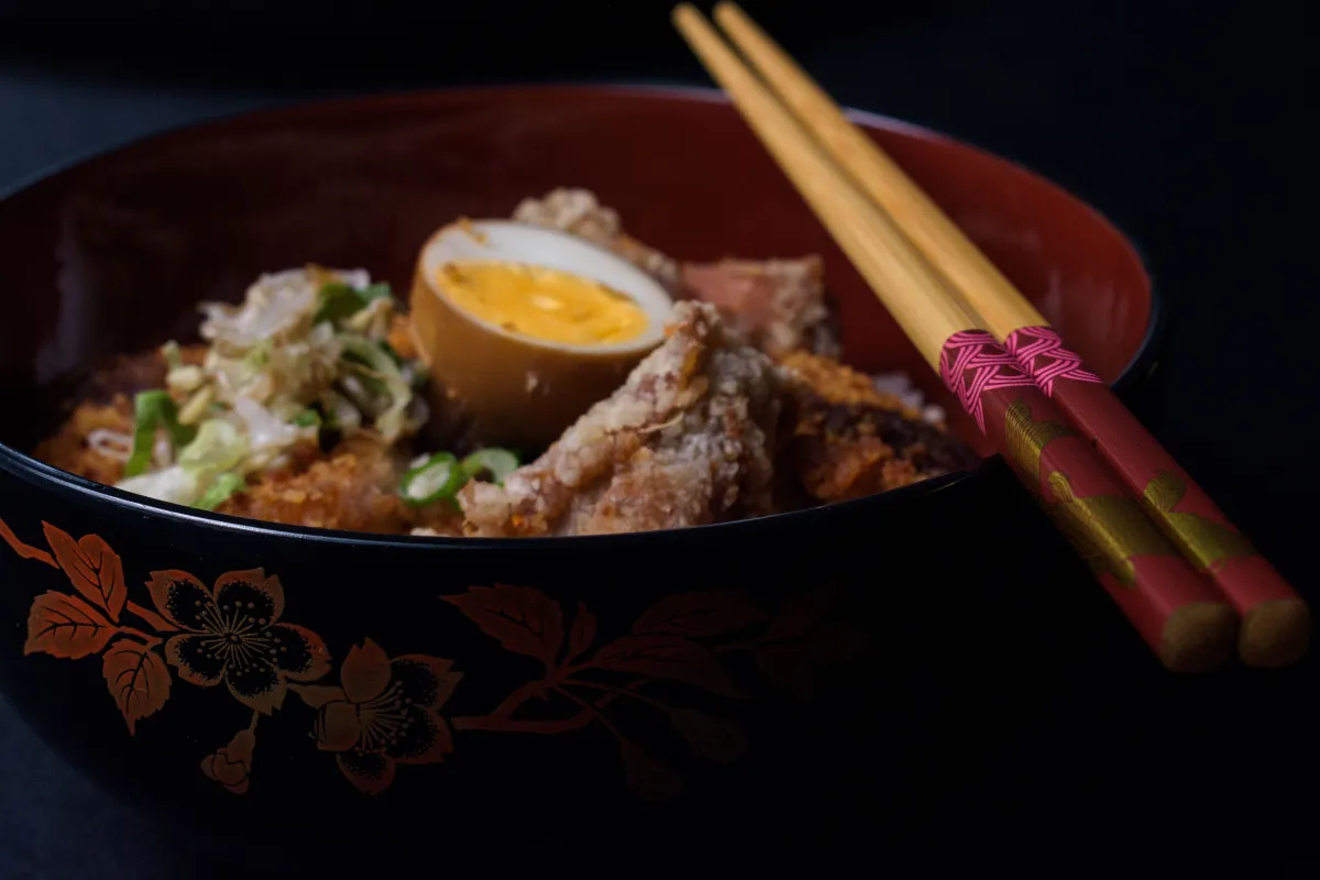 Steaming oyakodon in a ceramic bowl showing tender chicken, soft egg, and scallions over white rice with chopsticks resting beside.