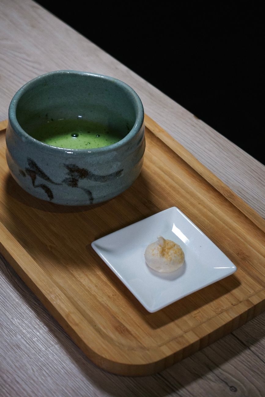 Traditional Japanese tea room with tatami mats, scroll hanging in tokonoma alcove, and ceramic tea bowl placed before seated guests.