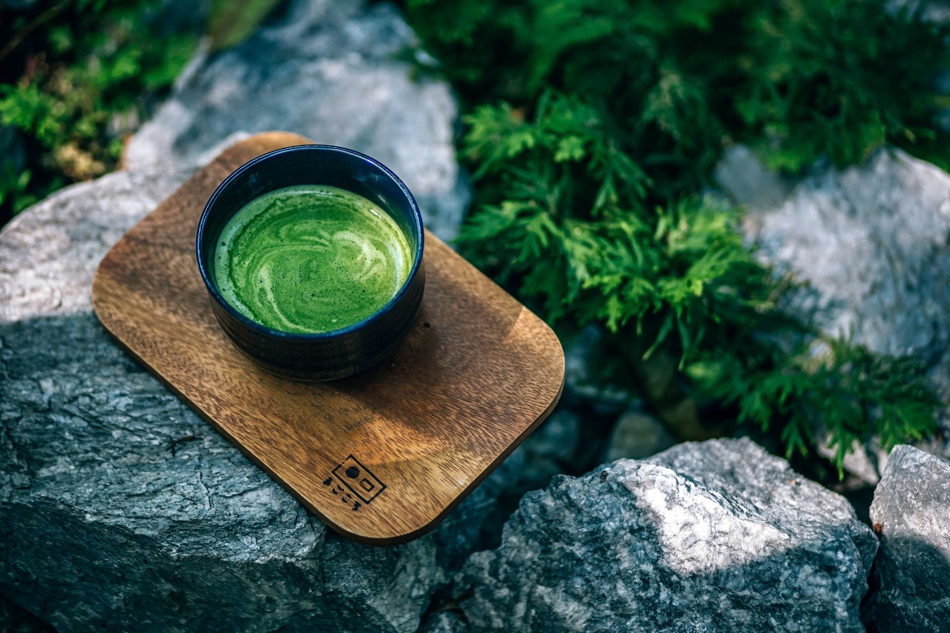 Bamboo chasen whisk creating foam in a ceramic bowl filled with vibrant green matcha tea on wooden surface
