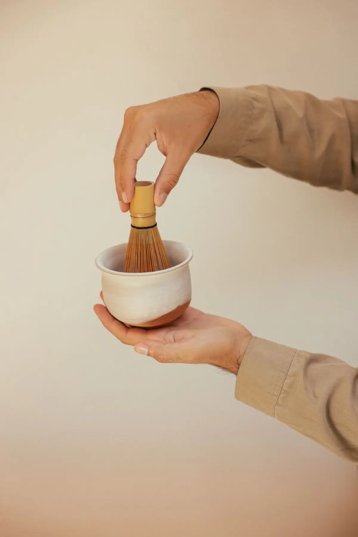 Bamboo chasen whisk creating foam in a ceramic bowl filled with vibrant green matcha tea on wooden surface