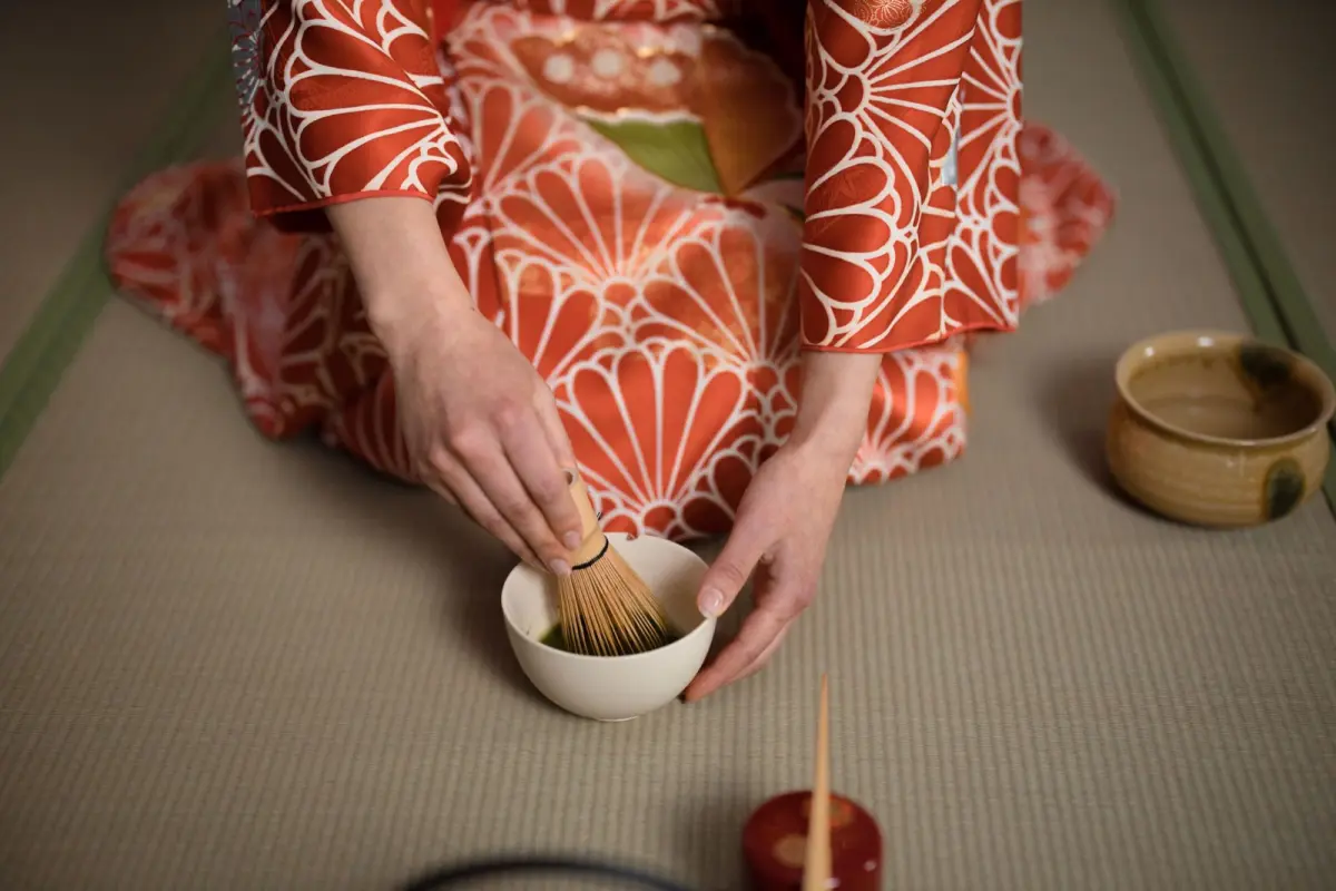 Bamboo chasen whisk creating foam in a ceramic bowl of vibrant green matcha tea with traditional preparation technique