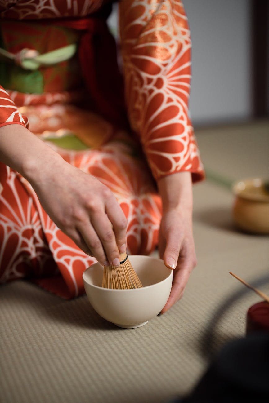 Bamboo chasen whisk creating foam in a ceramic bowl of vibrant green matcha tea with traditional preparation technique