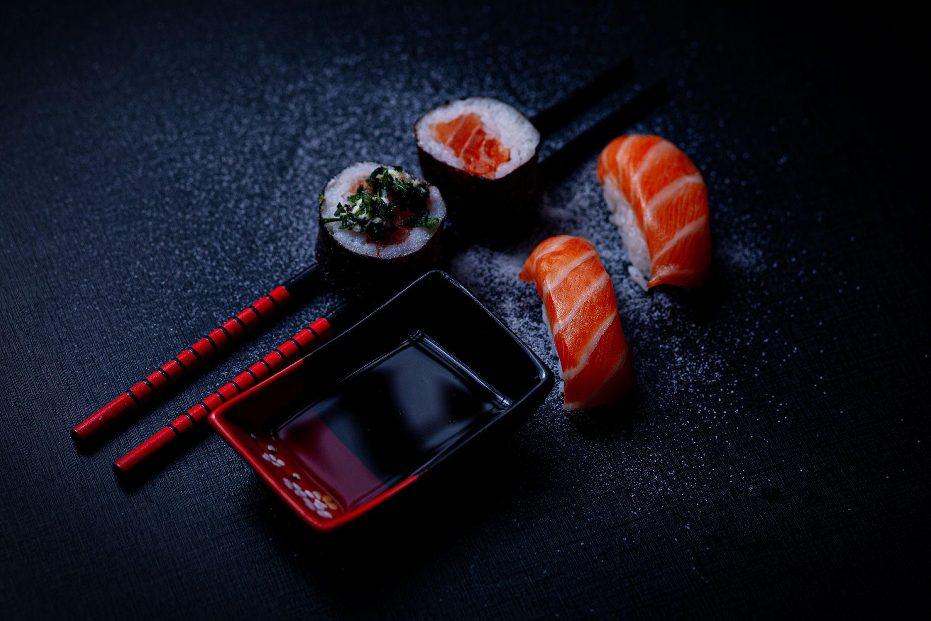 Nigiri sushi piece being gently dipped fish-side down into a small ceramic dish of dark soy sauce.