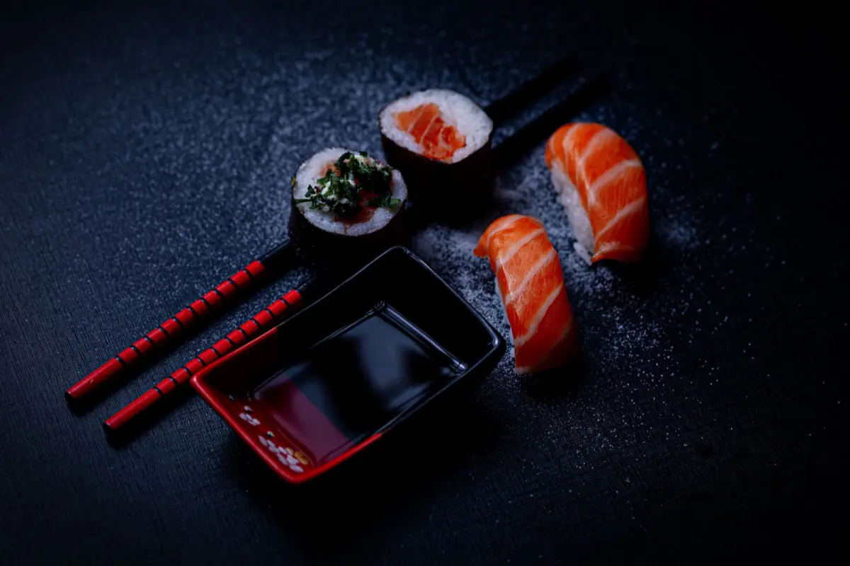 Nigiri sushi piece being gently dipped fish-side down into a small ceramic dish of dark soy sauce.