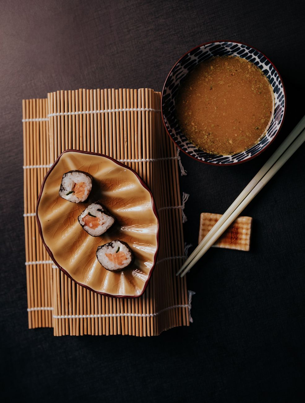 Nigiri sushi piece being gently dipped fish-side down into a small ceramic dish of dark soy sauce.