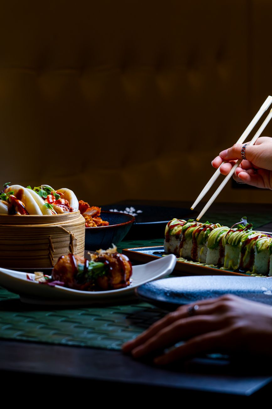 Side-by-side comparison showing shorter tapered Japanese chopsticks and longer blunt-tipped Chinese chopsticks resting on a wooden table.