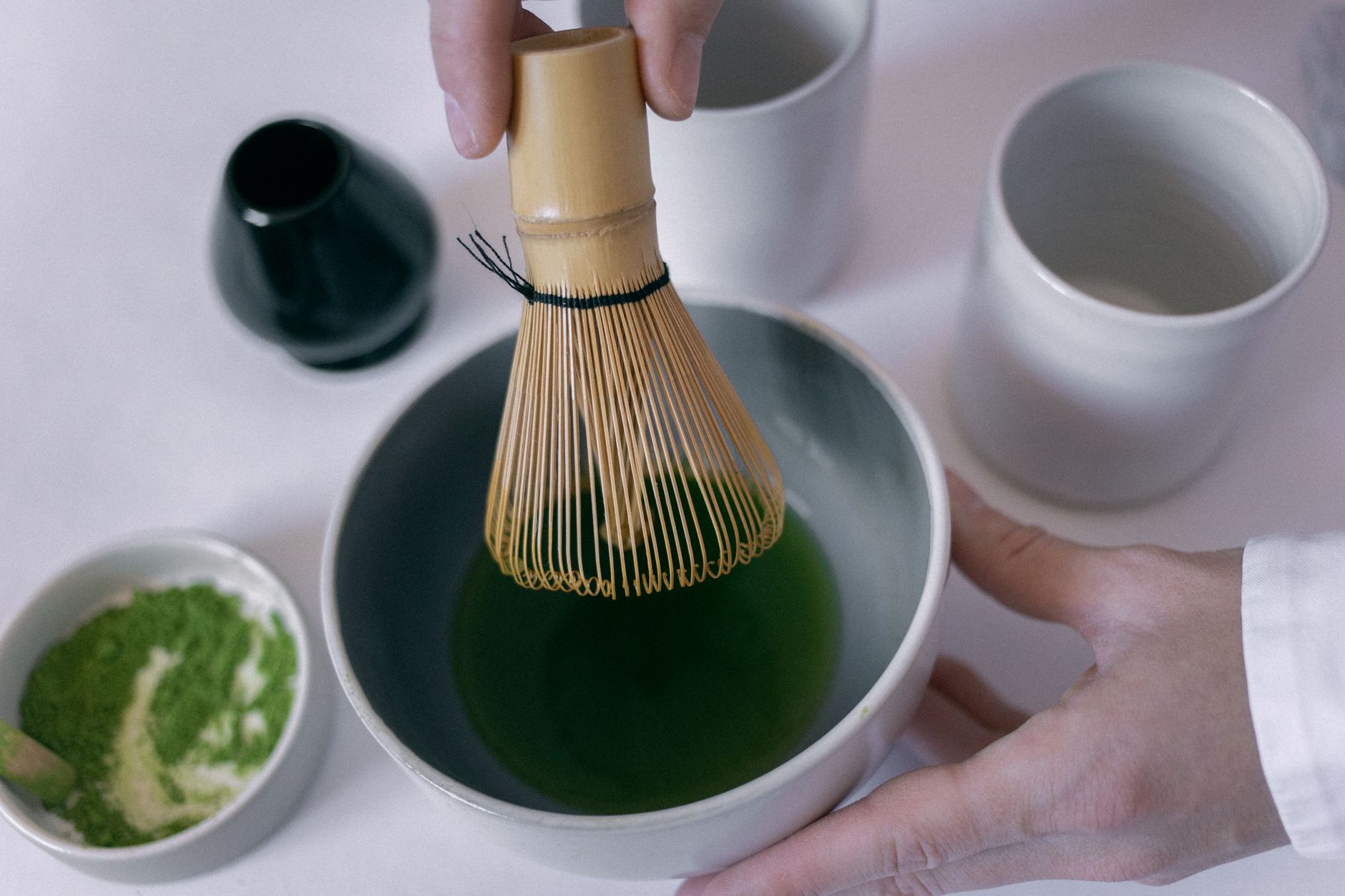 Bamboo chasen whisk creating foam in vibrant green matcha tea inside a traditional ceramic tea bowl.
