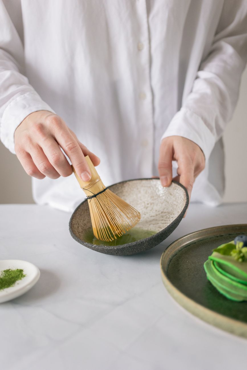 Bamboo chasen whisk creating foam in vibrant green matcha tea inside a traditional ceramic tea bowl.