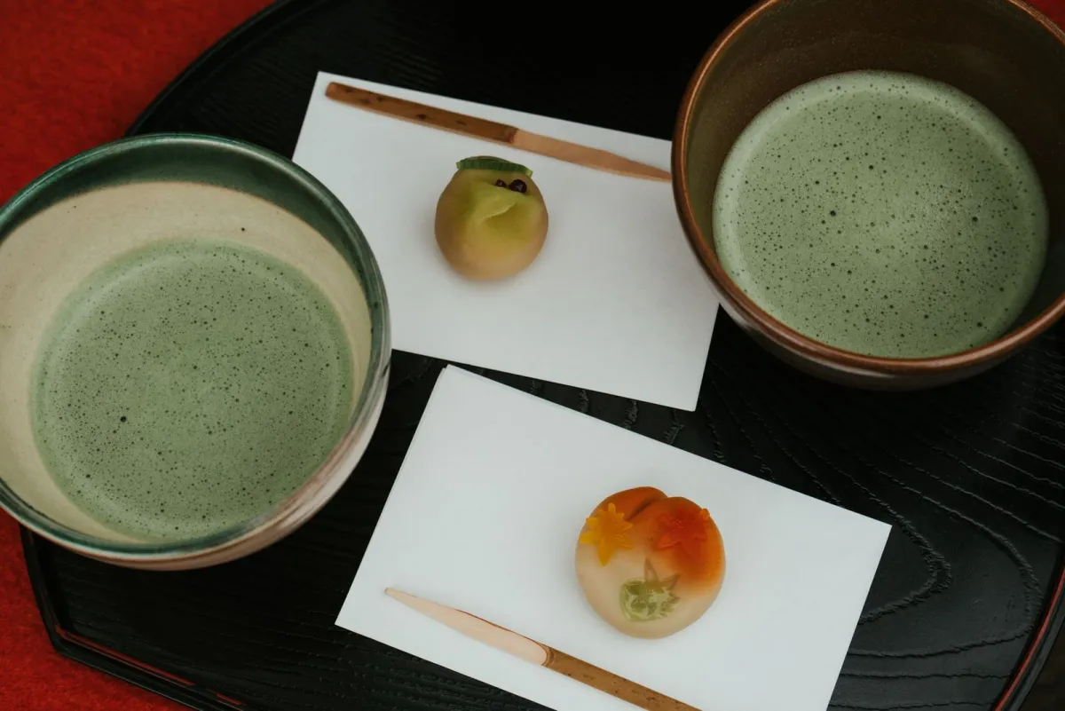 Traditional Japanese matcha tea in a black ceramic bowl beside pink sakura wagashi on a lacquered tray