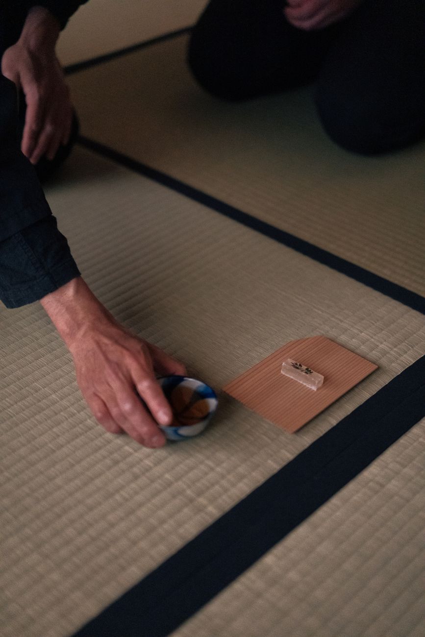 Guest's hands gently rotating a ceramic tea bowl clockwise to admire its decorative front before drinking matcha.