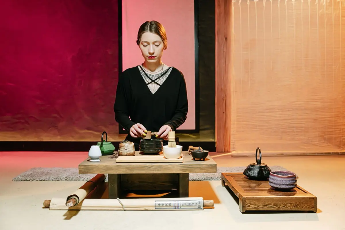 Guest in kimono bowing deeply on tatami mat before entering traditional Japanese tea room with sliding shoji doors.