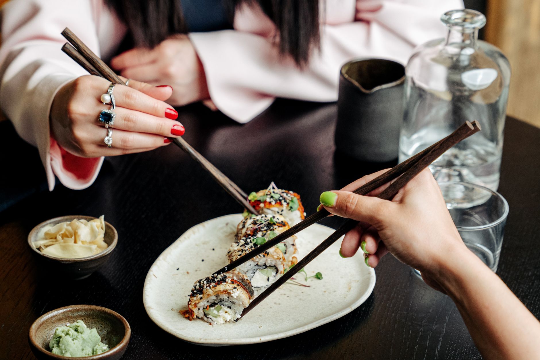 Artisan's hands applying fine gold powder to lacquered chopsticks using a delicate brush in traditional maki-e technique.