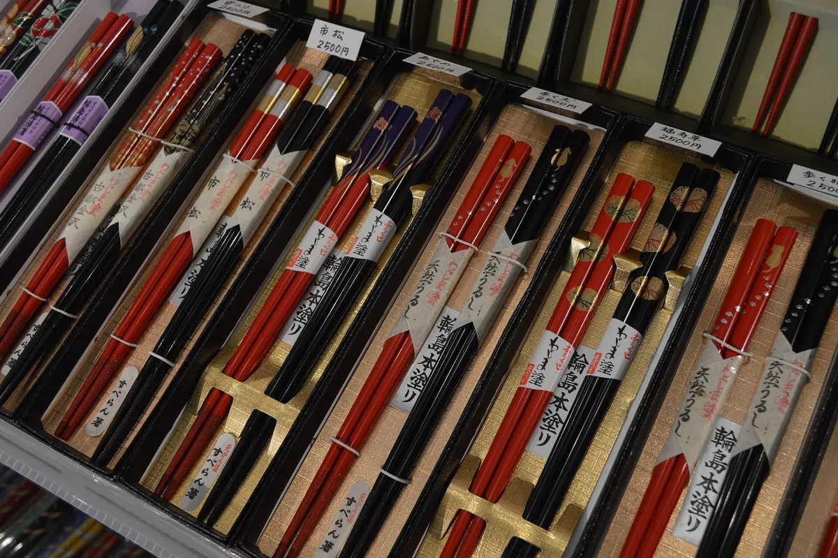 Artisan's hands applying fine gold powder to lacquered chopsticks using a delicate brush in traditional maki-e technique.