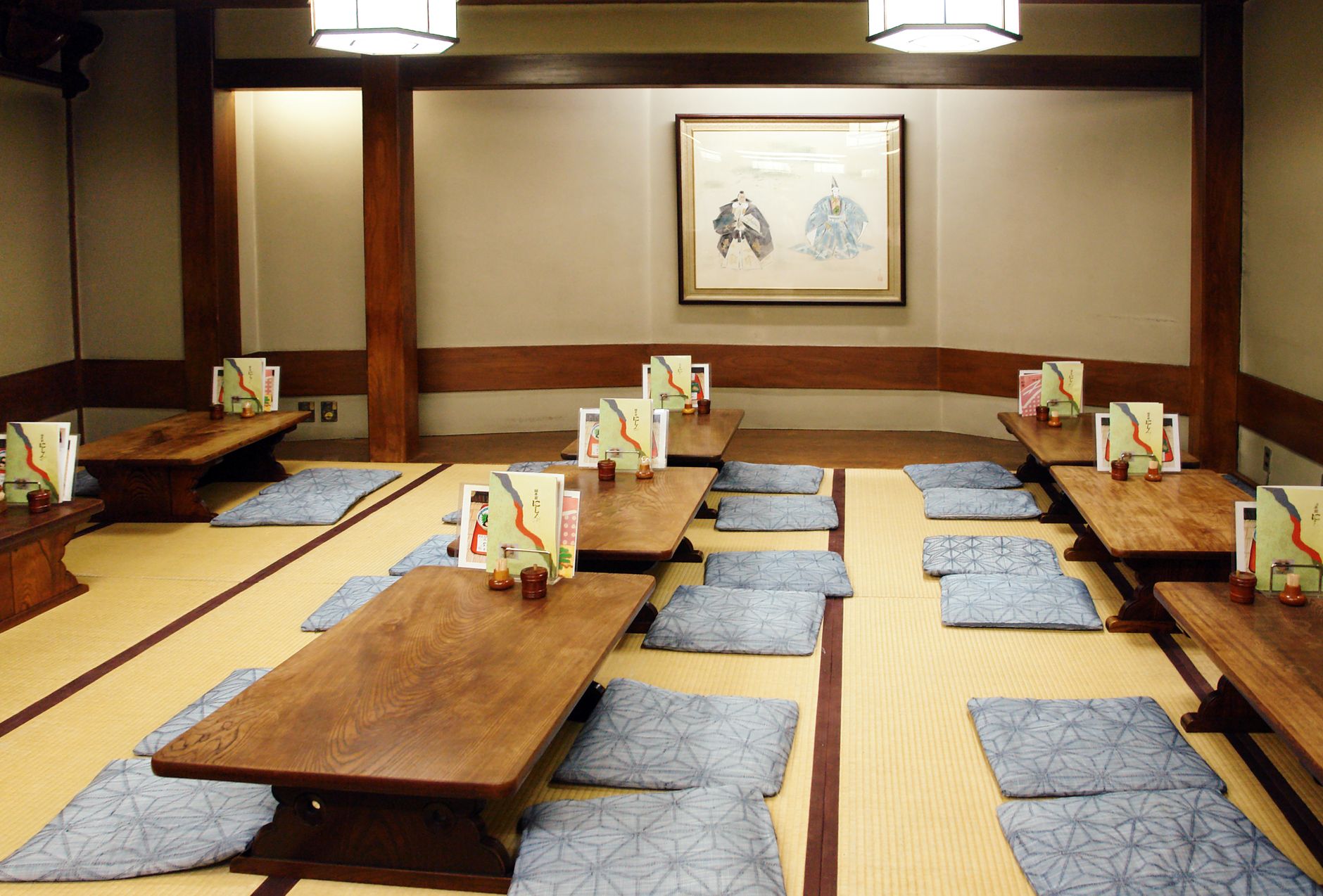 A wooden chabudai low table on tatami mats with cushions arranged around it in a traditional Japanese room
