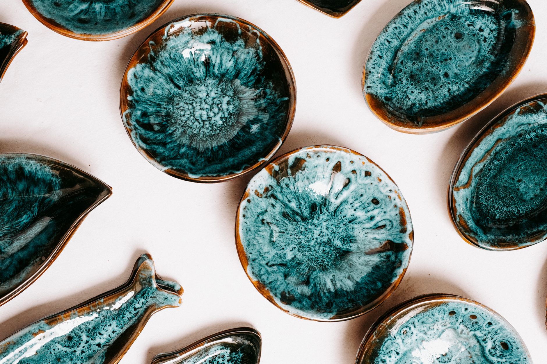Hands cradling an unglazed ceramic tea bowl with visible clay texture beside a glossy glazed dish on a wooden table