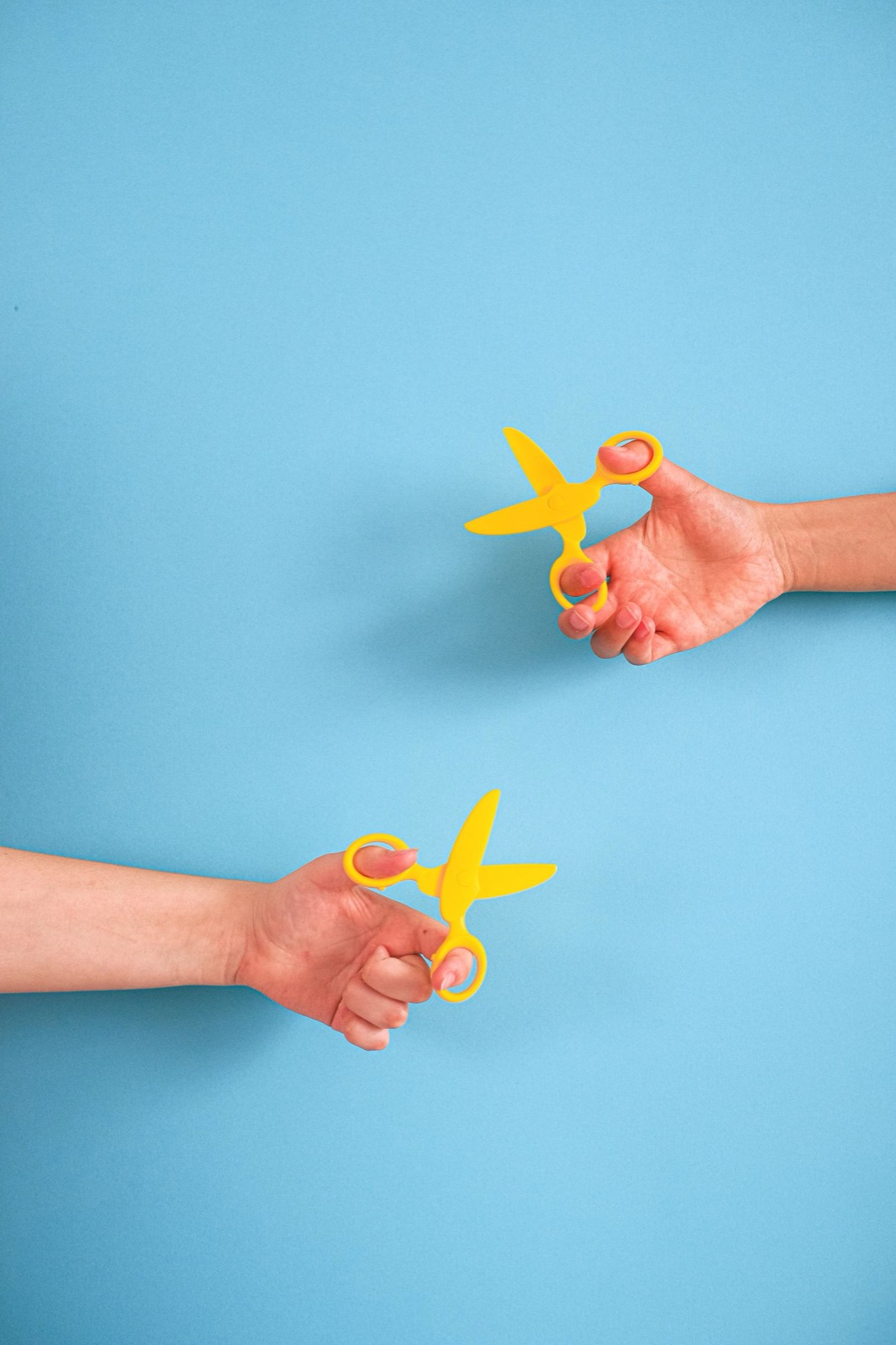 Hands presenting a pair of scissors with blades facing inward and handles extended outward in traditional Japanese manner