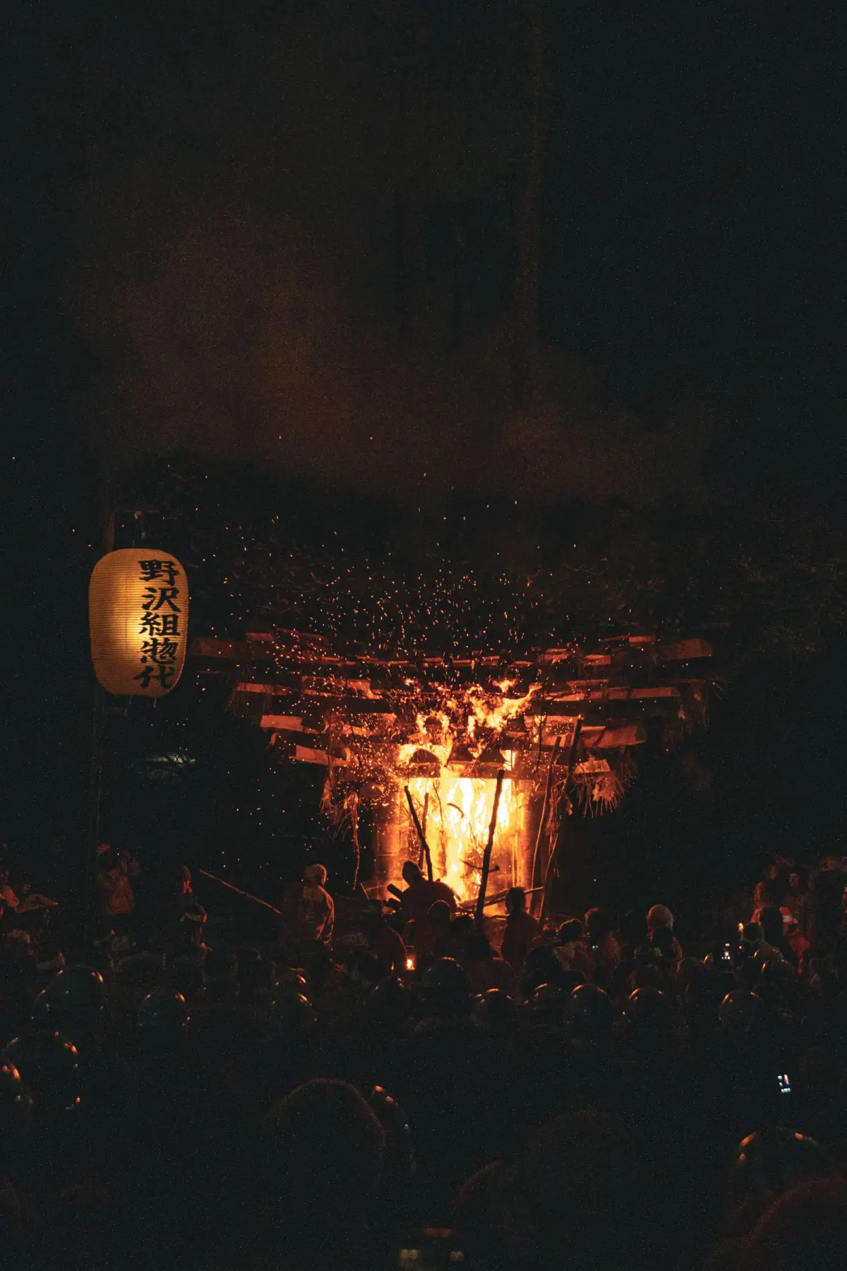 Massive pine torches illuminating a narrow mountain street during Kurama Fire Festival at night, with participants in traditional white garments.
