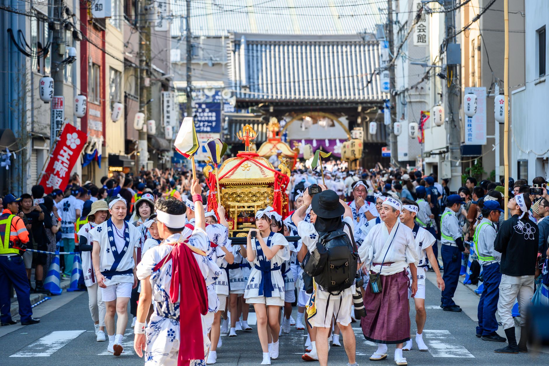 Golden mikoshi portable shrine carried through a Japanese festival street by people in traditional happi coats