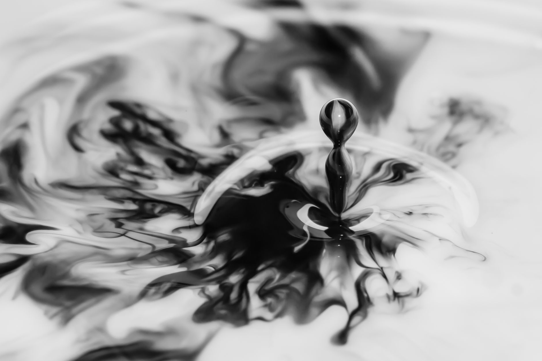 Marbled ink patterns floating on the surface of still water, captured mid-swirl in black and gray tones