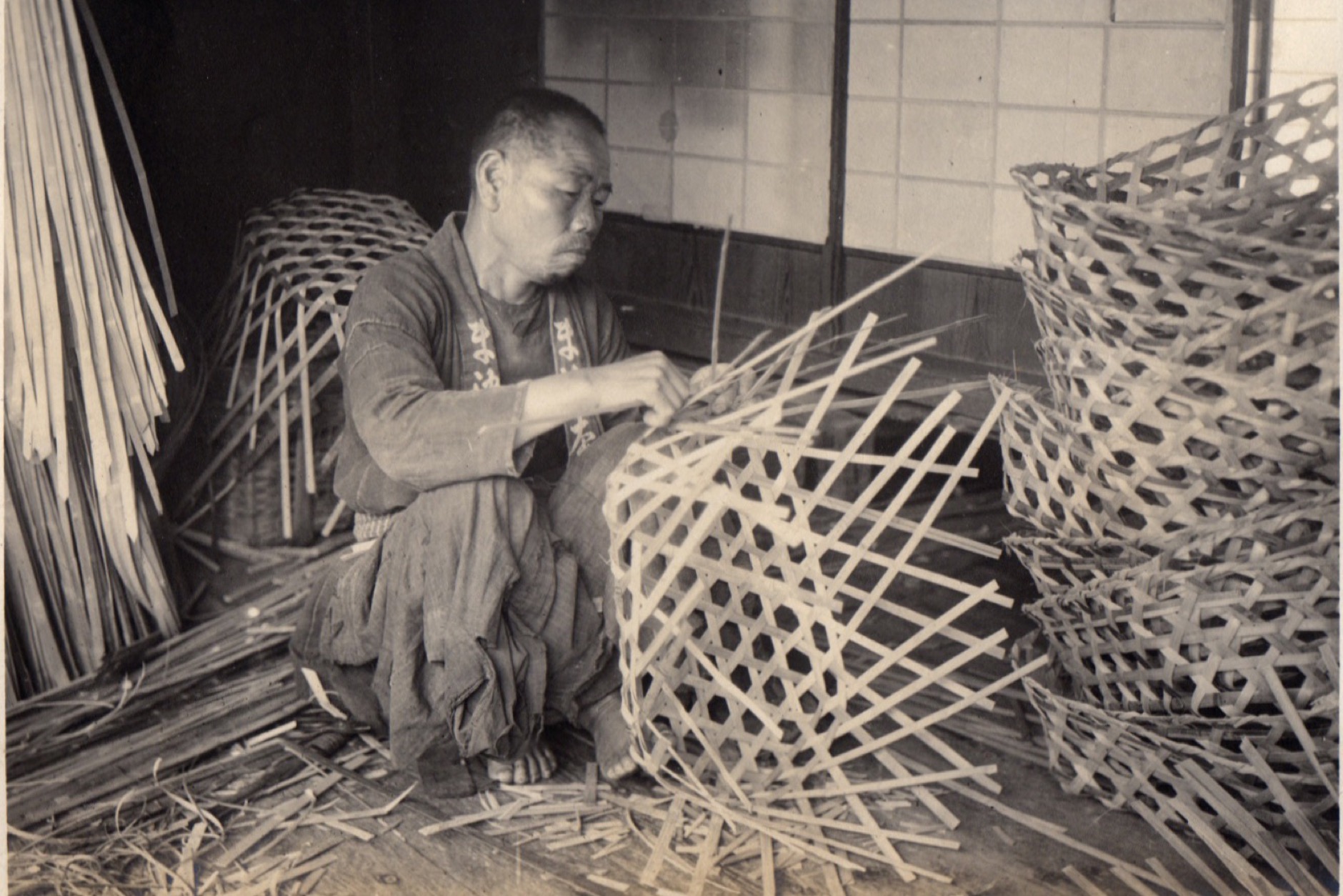 Artisan hands weaving thin bamboo strips into an intricate basket pattern in a traditional Japanese workshop
