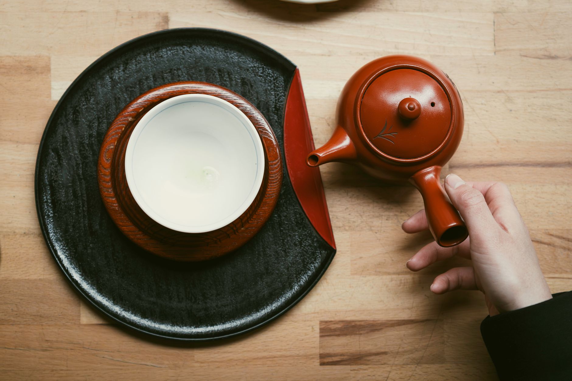 Artisan applying translucent urushi lacquer with a fine brush onto a wooden bowl in a traditional Japanese workshop.