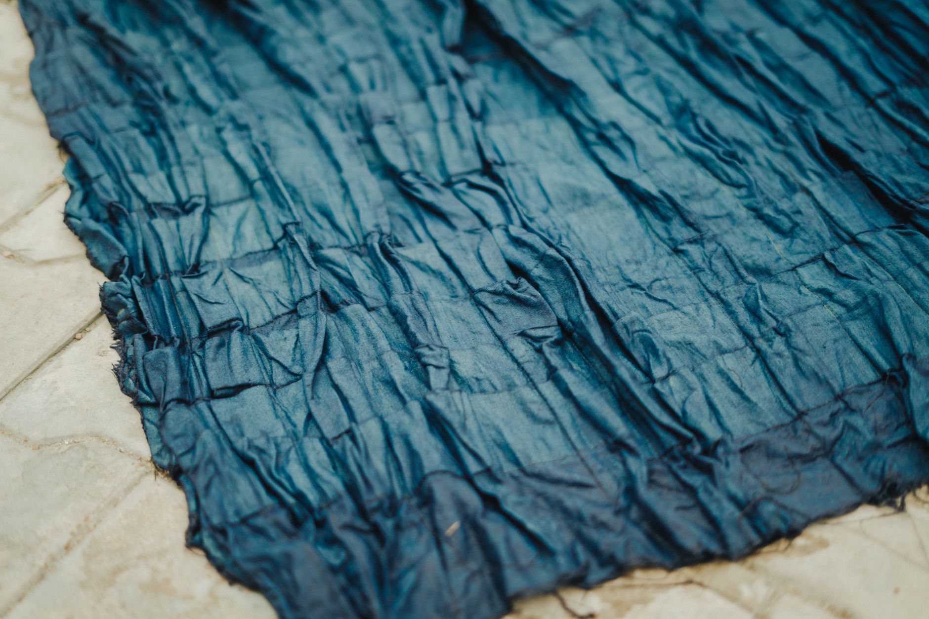 Artisan's hands submerging white cotton fabric into a deep blue indigo dye vat in a traditional Japanese workshop.