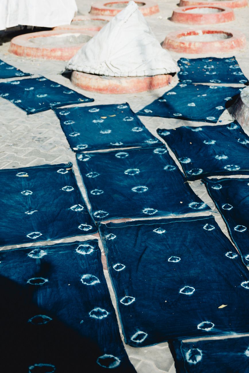 Artisan's hands submerging white cotton fabric into a deep blue indigo dye vat in a traditional Japanese workshop.